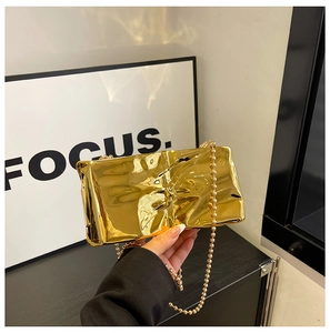Detalle de bolso de noche de acrílico dorado con textura de pliegues y cadena de perlas