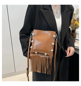 Detailed view of brown patent leather bucket bag with silver rivets and long fringes