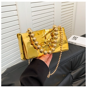 Detalle de bolso clutch de acrílico espejo dorado con asa de cuentas grandes y cadena