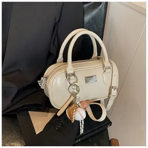 Detail view of a cream mini bowling bag with shiny finish and baseball keychain charm