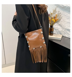 Detail of brown leather crossbody bucket bag with silver studs and long fringe tassels