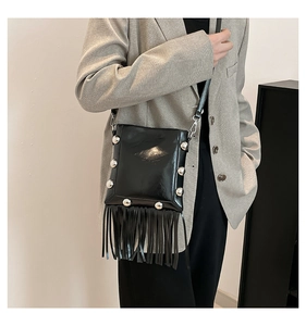 Detail of black patent leather bucket bag featuring silver rivets and long fringe tassels