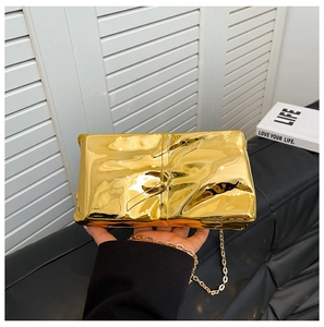 Detalle de bolso de mano metalizado dorado con textura plisada y correa de cadena