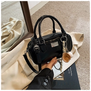 Detail of black glossy Boston bag with dual handles and baseball glove charm accessory