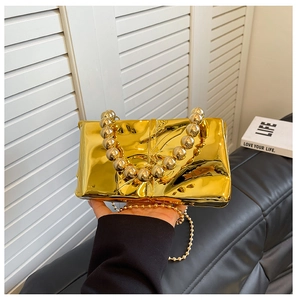 Detalle del bolso de espejo dorado con asa de cuentas y cadena metálica elegante
