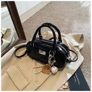 Detail of black glossy bowler bag with silver hardware on a beige blazer background