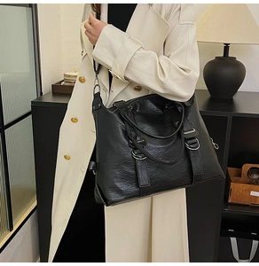 Detail of a large black leather tote bag worn with a stylish trench coat in an office setting