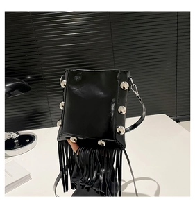 Detail of black crossbody bucket bag featuring silver studs and long leather tassels