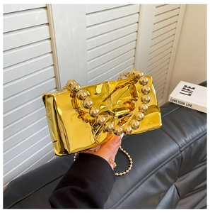 Detalle de un bolso de noche de acrílico dorado con asas de cuentas metálicas grandes