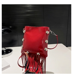 Macro shot of red patent leather bucket bag featuring silver rivets and long tassel details