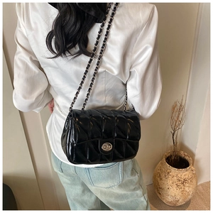 Détail d'un sac bandoulière matelassé noir avec chaîne argentée porté par un modèle