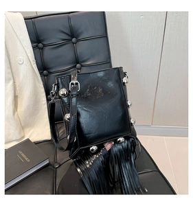 Detail of black patent leather bucket bag with silver studs and long fringes on a chair