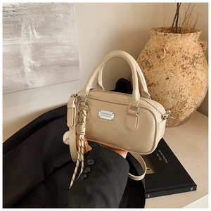 Detailed view of cream Boston bag with silver metal plate and woven rope charm