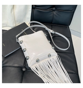 Close-up of white tassel bucket bag with silver studs on a dark leather background