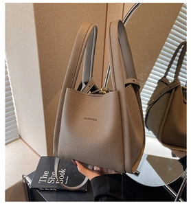 Detail of khaki pebbled leather bucket bag with top handles and logo in lifestyle setting