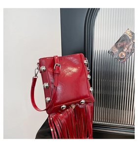 Detail of red glossy patent leather bucket bag featuring silver rivets and long tassels