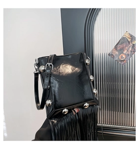 Detail view of black glossy leather bucket bag with long tassels and silver metal rivets
