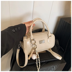 Close-up of cream bowling bag with metallic logo plate and sporty baseball pendant