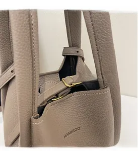 Detailed close-up of golden buckle and embossed logo on taupe lychee leather bucket bag