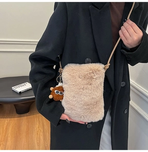 Close-up of beige plush crossbody bag with a funny brown monster pendant detail