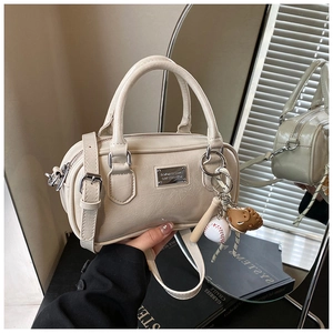 Macro detail of beige patent leather bowling bag with silver plaque and baseball charm