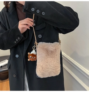 Detail of plush faux fur crossbody phone bag featuring a cute monster charm and strap