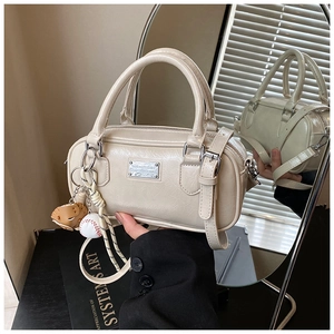 Detail of cream Boston barrel bag with silver logo plate and baseball glove charm