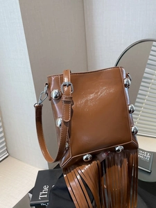 Brown glossy vintage bucket bag with silver studs and long tassels in a stylish room setup
