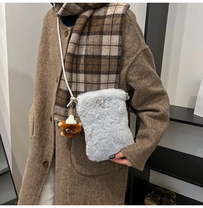 Detail showing plush light gray crossbody bag with a brown bear doll charm and strap