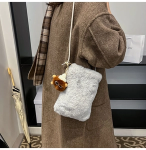 Detail of gray plush crossbody bag with cute monkey charm and stylish cream strap