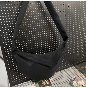 Detail of minimalist black nylon crescent bag featuring wide strap and zipper closure