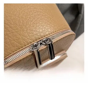 Macro detail of silver metal dual zippers and textured lychee leather on a beige backpack