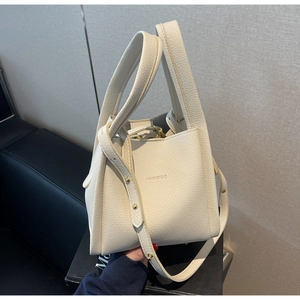 Detail view of lychee pattern cream leather bucket bag with gold hardware and brand logo