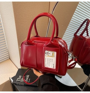 Close-up of red glossy shoulder bag featuring cartoon puppy card detail and sleek handles