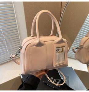 Detailed mirror shot of a light pink glossy bowling bag with double handles and strap
