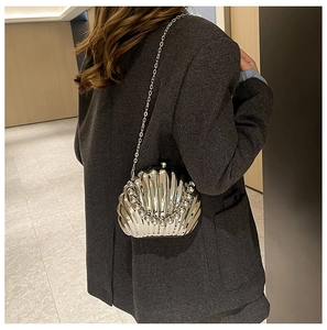 Close-up of a silver shell-shaped crossbody bag with bead handle on a grey suit model