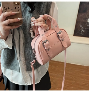 Mini sac Boston rose avec boucles argentées et bandoulière réglable tenu à la main