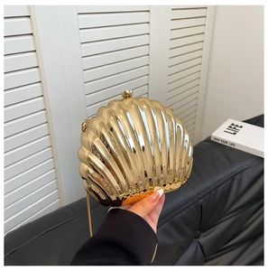 Handheld view of a gold shell-shaped evening clutch with metallic texture and acrylic chain