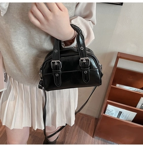 Détail d'un mini sac Boston noir en cuir brillant porté en bandoulière pour femme