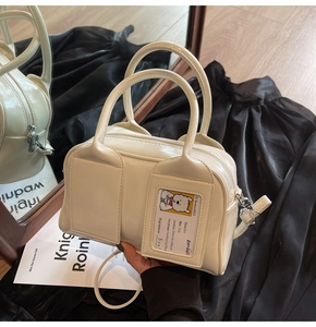Detail of cream patent leather bowling bag featuring reinforced dual handles and card slot