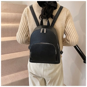 Detailed back view of a black pebbled leather backpack worn by a model on stairs