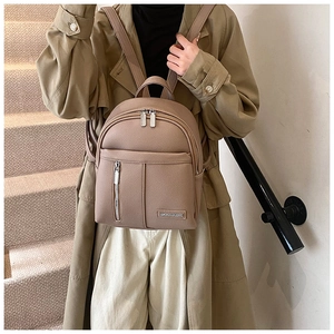 Detail of beige lychee textured PU leather backpack with silver zippers and metal tag