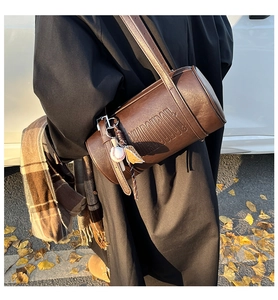 Close-up of dark brown cylindrical leather bag with embossed letters and baseball charm