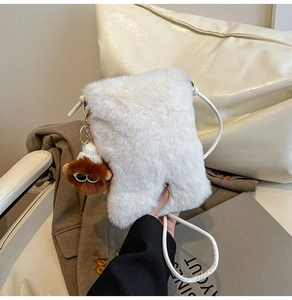 Close-up of white plush crossbody bag with quirky brown monster charm and thin strap
