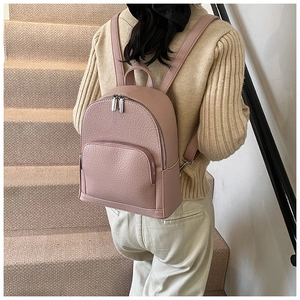 Detail of pink pebbled leather backpack with silver zippers worn over a beige sweater