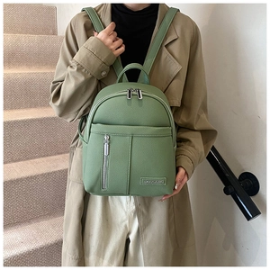 Detail of light green pebbled leather backpack with dual zippers and metal logo plate