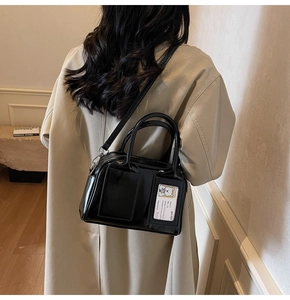 Detail of black patent leather bowling bag worn as crossbody with polished silver hardware