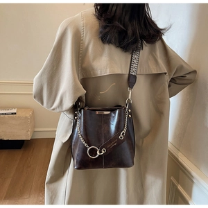 Détail du sac seau marron foncé brillant avec chaîne dorée et large bandoulière ethnique
