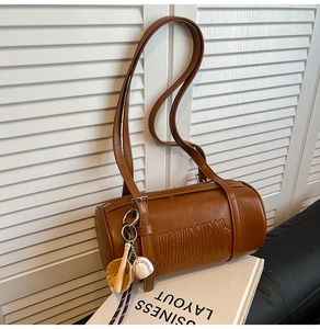 Detail of vintage brown cylinder shoulder bag with embossed letters and baseball charm