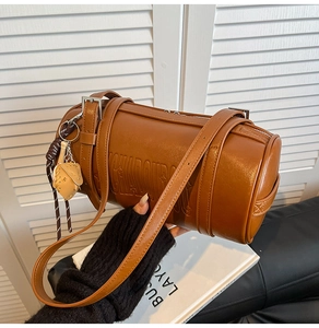 Detail of brown barrel shoulder bag with letter embossing and baseball glove charm